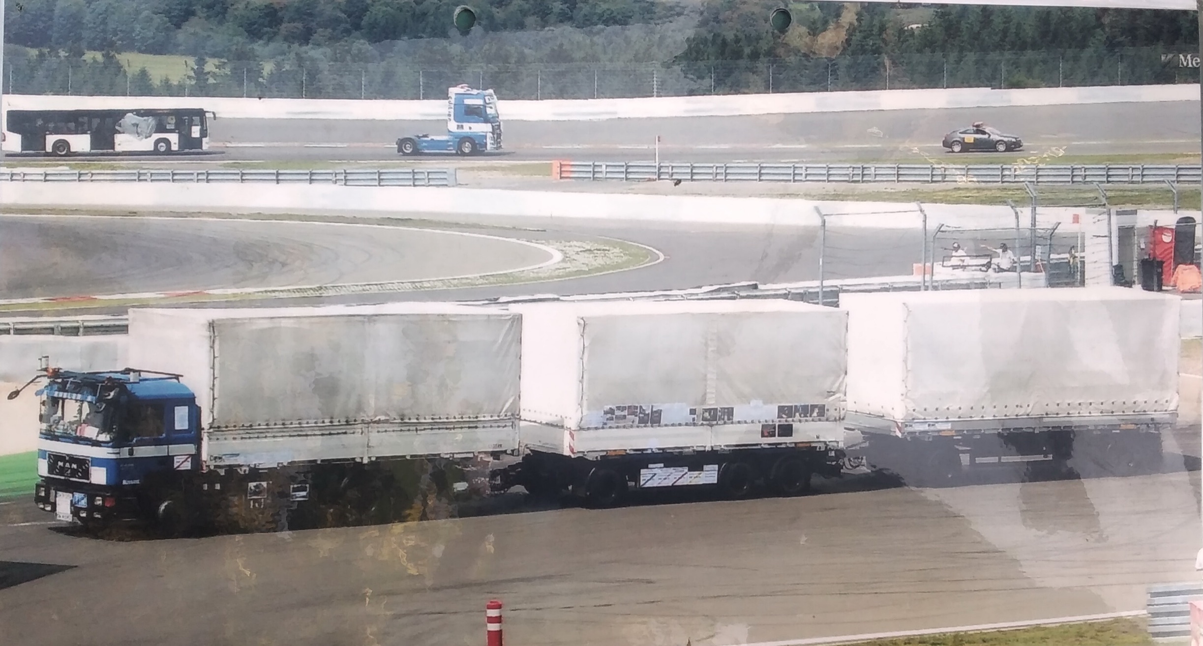 Blauer LKW mit drei Planenaufbauten hintereinander auf einer Rennstrecke